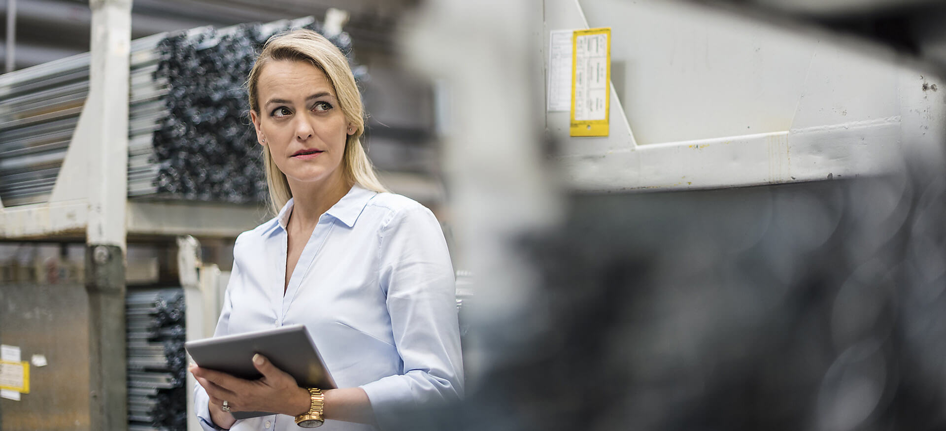 Blonde Frau hält Tablet in Hochregallager.